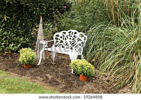 White wrought iron bench in a garden setting surrounded by fall mums