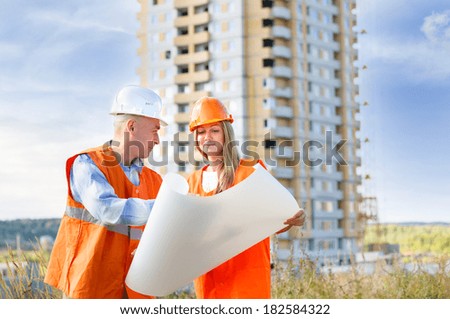female male builders wearing helmets on the background of a house under construction