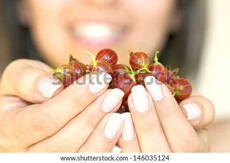 Ripe gooseberry in woman's hands in foreground and smiling woman face in background