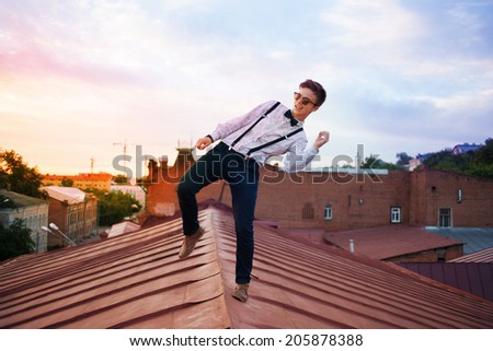 Young bold girl woman hipster jumping on the roof, dressed like a boy man in a shirt, bow-tie, suspenders and pants trousers