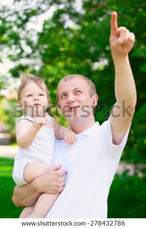 Father dad parent holding baby boy outdoors in summer garden pointing something in sky