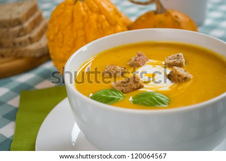 Pumpkin soup in a white plate with cream and bread