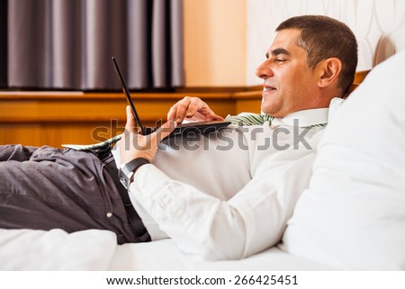 Businessman lying in bed and surfing the net on laptop