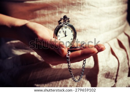 Woman holding antique watch that shows five to twelve time, intentionally toned.