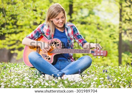Young woman sitting in park and tuning acoustic guitar