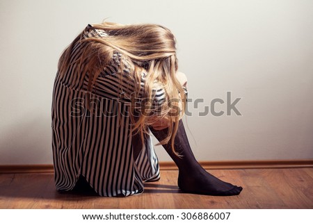 Young woman in despair sitting on floor, intentionally toned