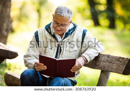 Happy senior man reading book in park in autumn day
