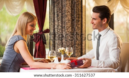 Happy couple at the restaurant, man is giving present to his girlfriend