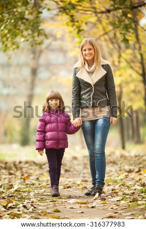 Mother and daughter walking in park in autumn