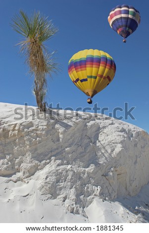 two colorful hot air balloons floating over a sand wall and yucca at white sands natl. monument