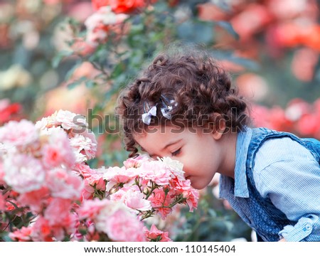 Portrait of a two year old little girl outdoor in a rose garden smelling the flowers.