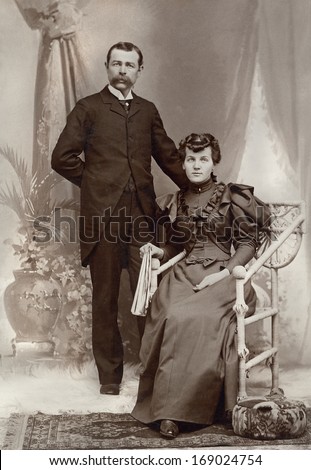 US - NEW YORK - CIRCA 1895 - A vintage antique photo of a young couple. The husband is standing while his wife is sitting in a chair. A photo is from the Victorian era. CIRCA 1895