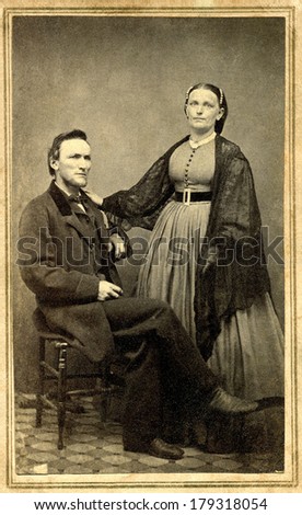 USA - CONNECTICUT - CIRCA 1865 A vintage cartes de visite photo of pioneer couple. Wife is standing and husband sitting. She is dressed in hoop skirt. Photo from Civil War Victorian era. CIRCA 1865