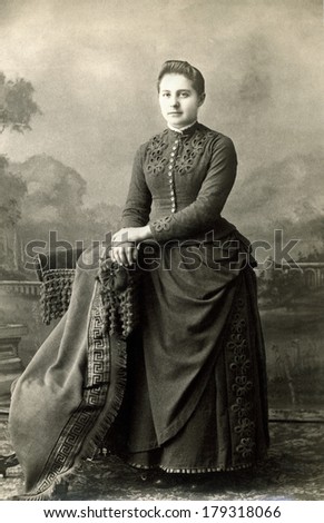 USA - NEW YORK - CIRCA 1885 A vintage cabinet card of a young woman dressed in a Victorian style bustle dress standing with her hands placed on a chair. Photo is from the Victorian era. CIRCA 1885
