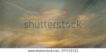 A beautiful sunset with a golden glow and blue sky and clouds. A textured grunge effect has been applied to make it look weathered and worn.