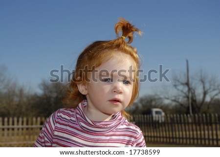 A red headed blue eyed little girl with her hair in a pony tail.