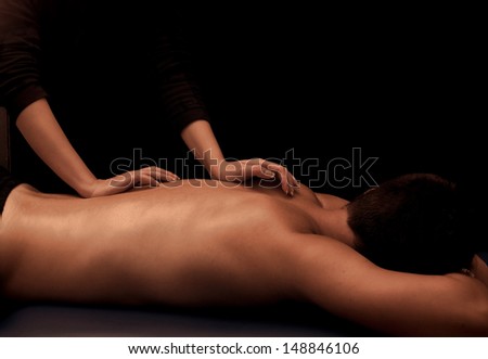 Man getting a back massage at spa, low key lighting with black background