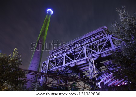 night shot of a metal factory with huge tower and moved sky