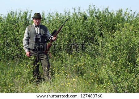hunter with rifle standing in bush