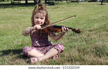 little girl sitting on grass and play violin