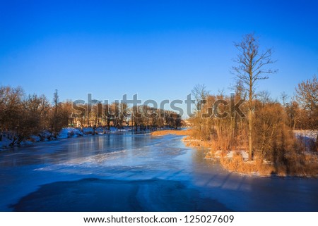 Winter river with ice on a surface and snowy coast under blue clear sky