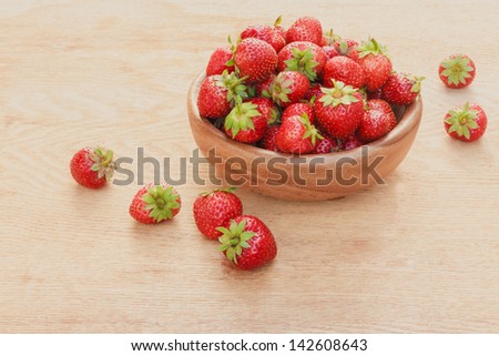 Old wooden bowl filled with succulent juicy fresh ripe red strawberries on an old wooden textured table top / Close-up of strawberries in vintage wooden bowl on wooden table