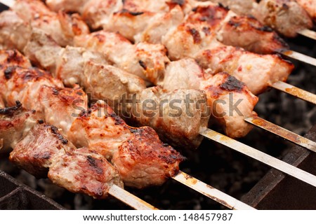Shish kebab in process of cooking on open fire outdoors / Juicy slices of meat with sauce prepare on fire (shish kebab)