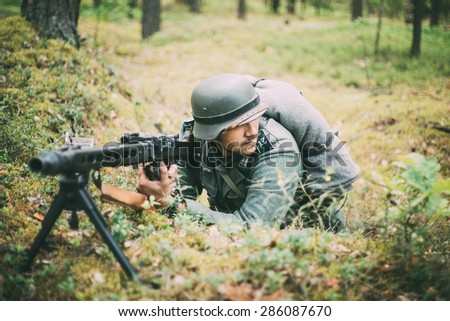 SVETLAHORSK, BELARUS - JUNE 20, 2014: Unidentified re-enactor dressed as German soldier machine-gunner aiming a machine gun at a enemy in summer forest.