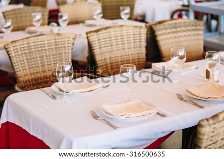 The cozy interior of summer cafe - sheltered tables with white tablecloths and wicker chairs. European town