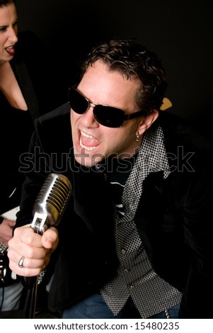 Close-up of male lead singer with retro mic and female guitar player in background