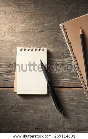 Small notepad with pen and pencil on rustic wood background with low key scene.