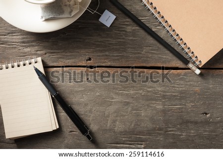 Small notepad with empty coffee cup, tea bag, pen and pencil on rustic wood background with low key scene
