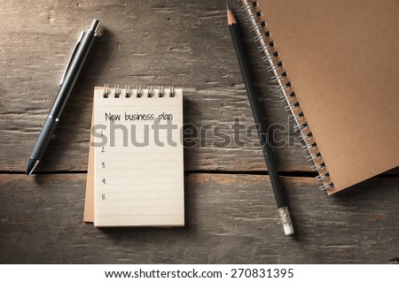 Small notepad with text, pen, and pencil on rustic wood background with low key scene.