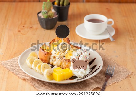 Honey toast with banana, whipped cream, chocolate chip ice cream, and mango jelly on white dish with black circle tag stab down on the ice cream in vintage scene