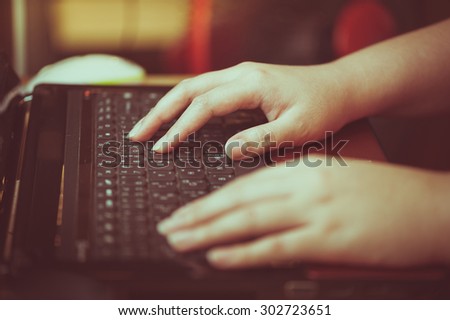 Female hand typing on laptop keyboard with film filter effect