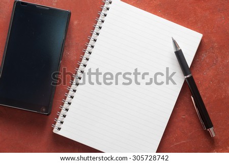 Opened notepad with pen and black smart phone on rustic cement background with low key scene.