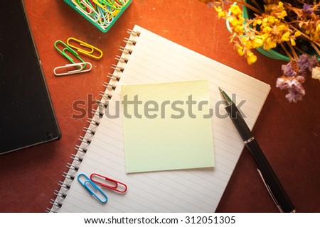Opened notepad with pen, small sticky paper, smartphone, and paper clips on red cement background with morning scene