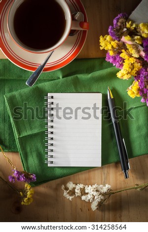 Opened notepad with pen and a cup of hot coffee on wood table in cafe with low key scene