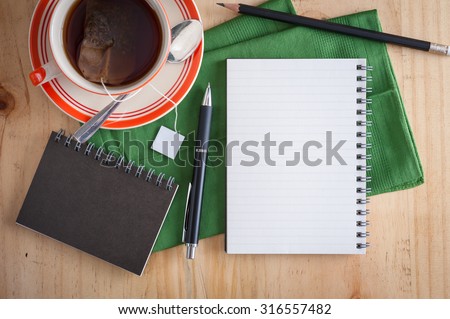 Opened notepad with pen and a cup of hot tea on wood table in cafe in morning scene with blank area for text or message