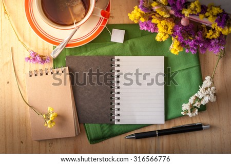 Opened notepad with pen and a cup of hot tea on wood table in cafe at morning time with blank area for text or message