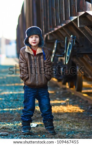 homeless Boy bum in brown jacket and a fur hat and crumpled jeans on the street near railway wagon
