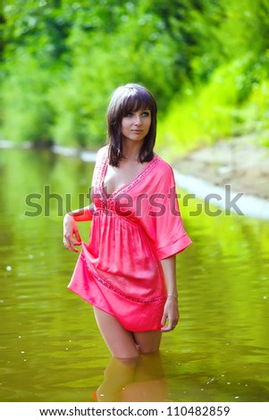 woman brunette in red dress is wet to the waist in the water touches the hand of river