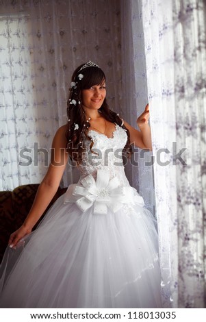 bride brunette woman standing at the window in the room on the wedding day