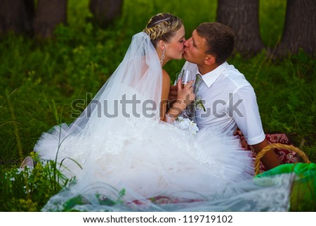 bride and groom at wedding in green forest sitting on picnic, drink from wine glasses at wedding