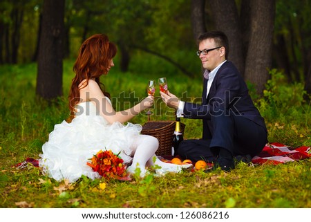 Russia newlyweds couple bride, and groom sitting on green grass, picnic in woods at wedding drink wine