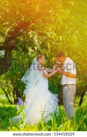 sunlight bride groom kissing hand of blonde bride, newlyweds couple are in a green forest in wedding summer