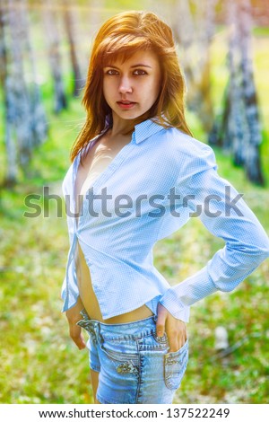 brunette in jeans and rastegnutaya shirt on a green background outdoors nature
