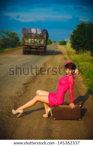 woman on the road sitting on a suitcase, retro travel photo travel passes behind a truck