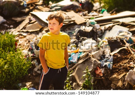 German homeless boy child is on garbage dump in a yellow T-shirt
