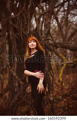 girl red-haired woman in black dress dry dark forest, dry branches on street